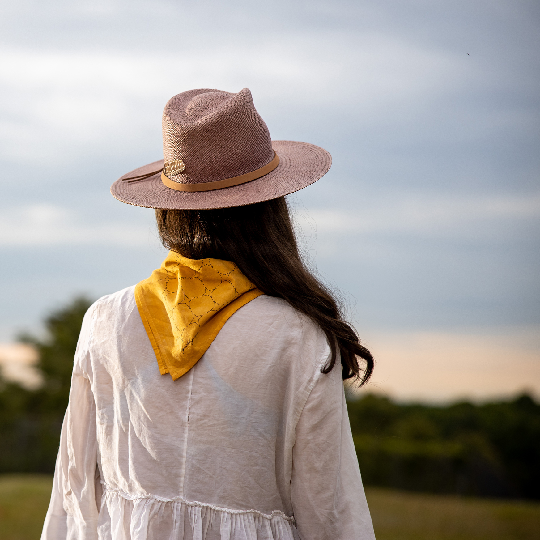 Woman looking into the sunset wearing a yellow bandana around her neck and a wide-brimmed hat