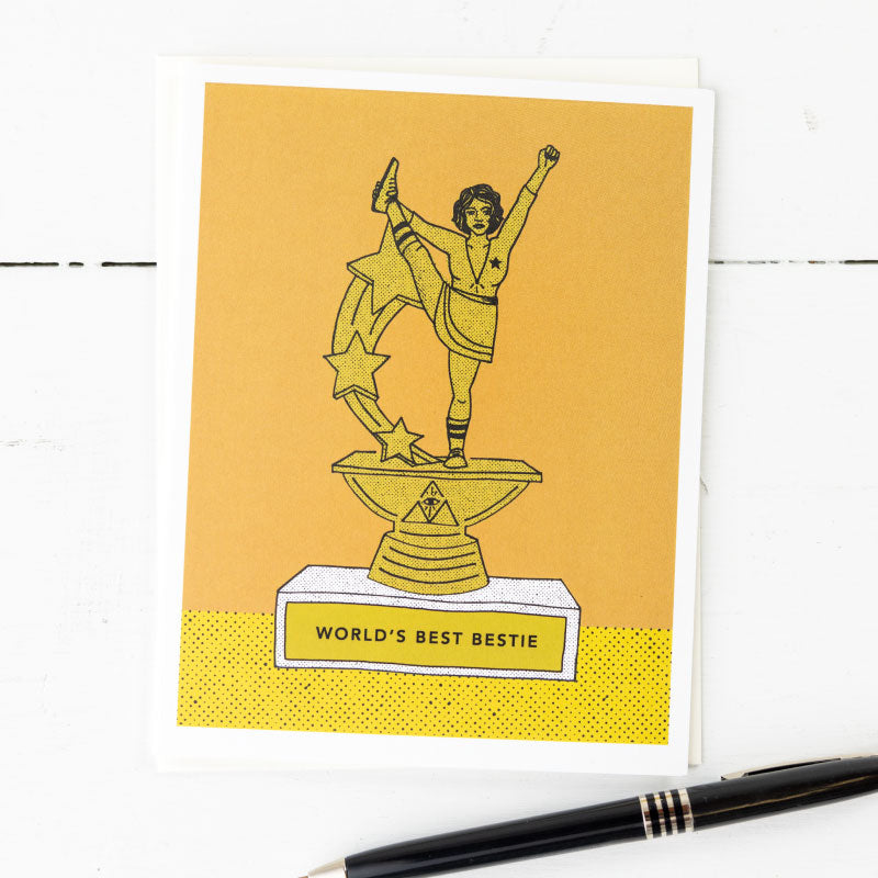 This image features a charming greeting card titled "World's Best Bestie," designed to celebrate a special friend. The card displays a vibrant, hand-illustrated trophy graphic on a mustard yellow background.