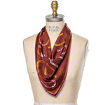 A maroon silk scarf with a pattern of horseshoes, keys, and musical notes, displayed on a mannequin.