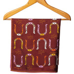 A maroon silk scarf with a pattern of colorful horseshoes displayed on a wooden hanger.