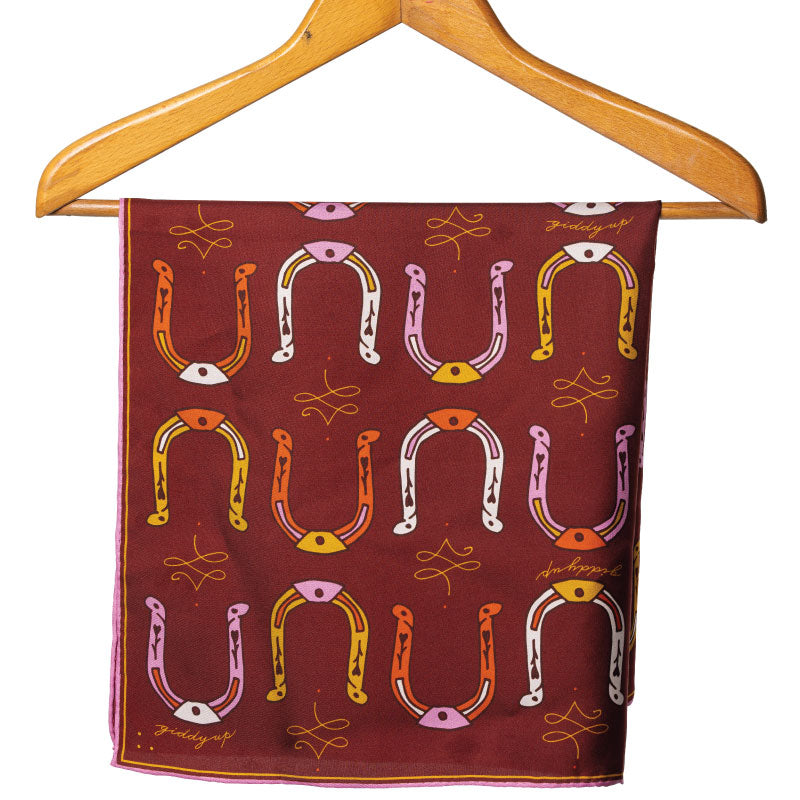 A maroon silk scarf with a pattern of colorful horseshoes displayed on a wooden hanger.