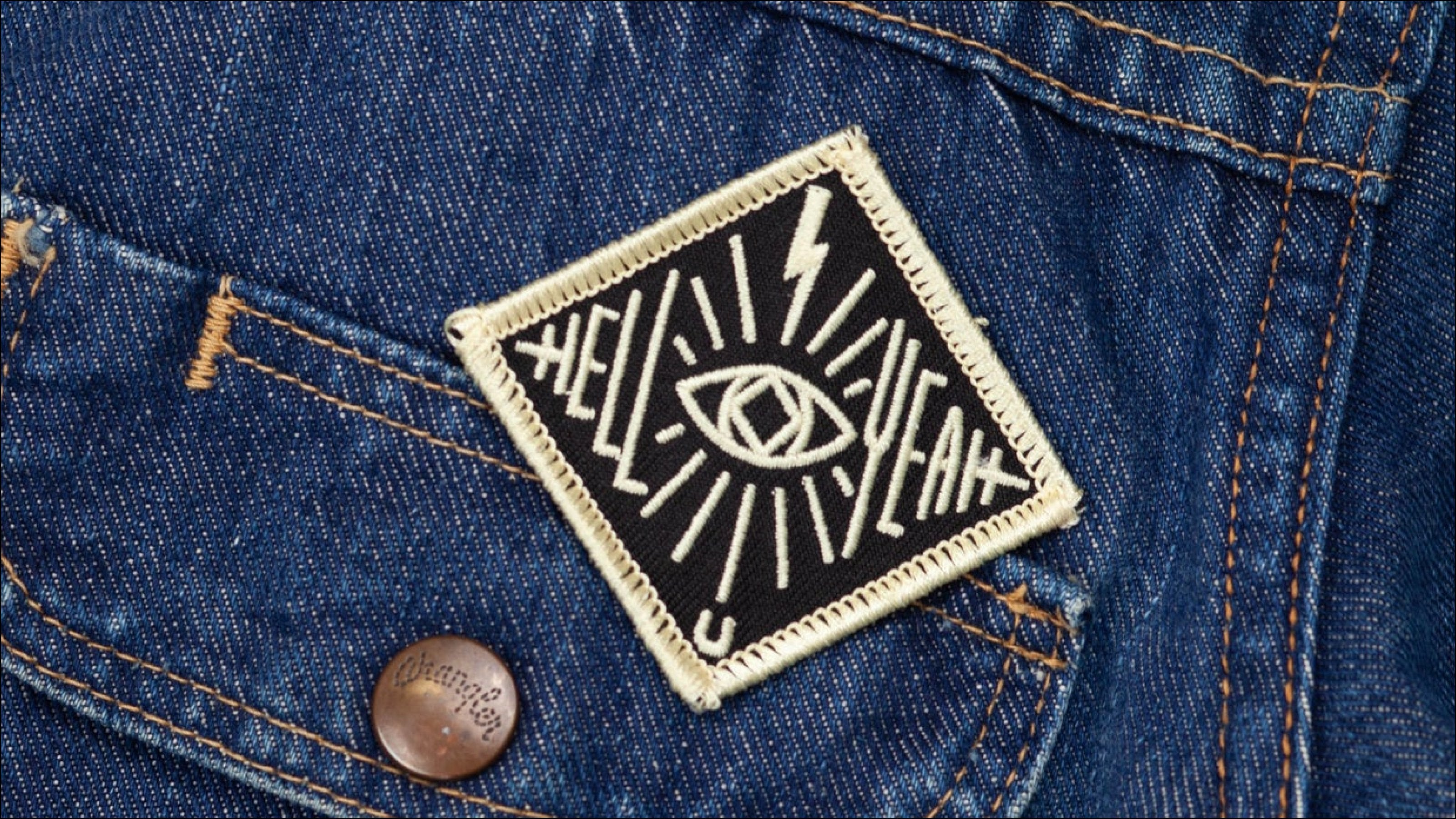 Close up of a Jenni Earle patch that says Hell Yeah in stylized font with an eye and lightning bolt illustration on a jean jacket pocket