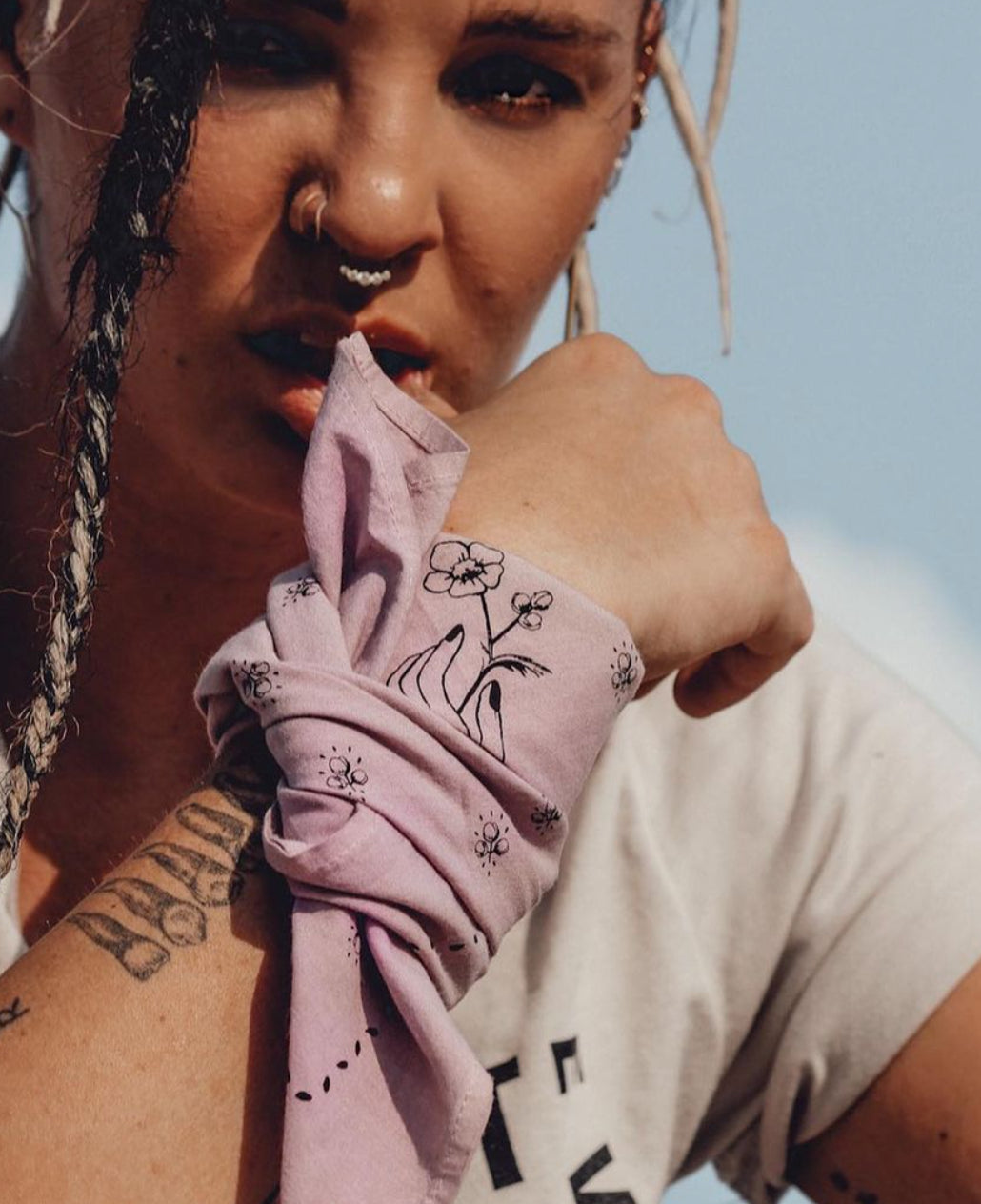 bipoc woman with nose ring and braids wearing a pink jenni earle bandana with flowers on it from the rebel collection tied around her wrist as a talisman