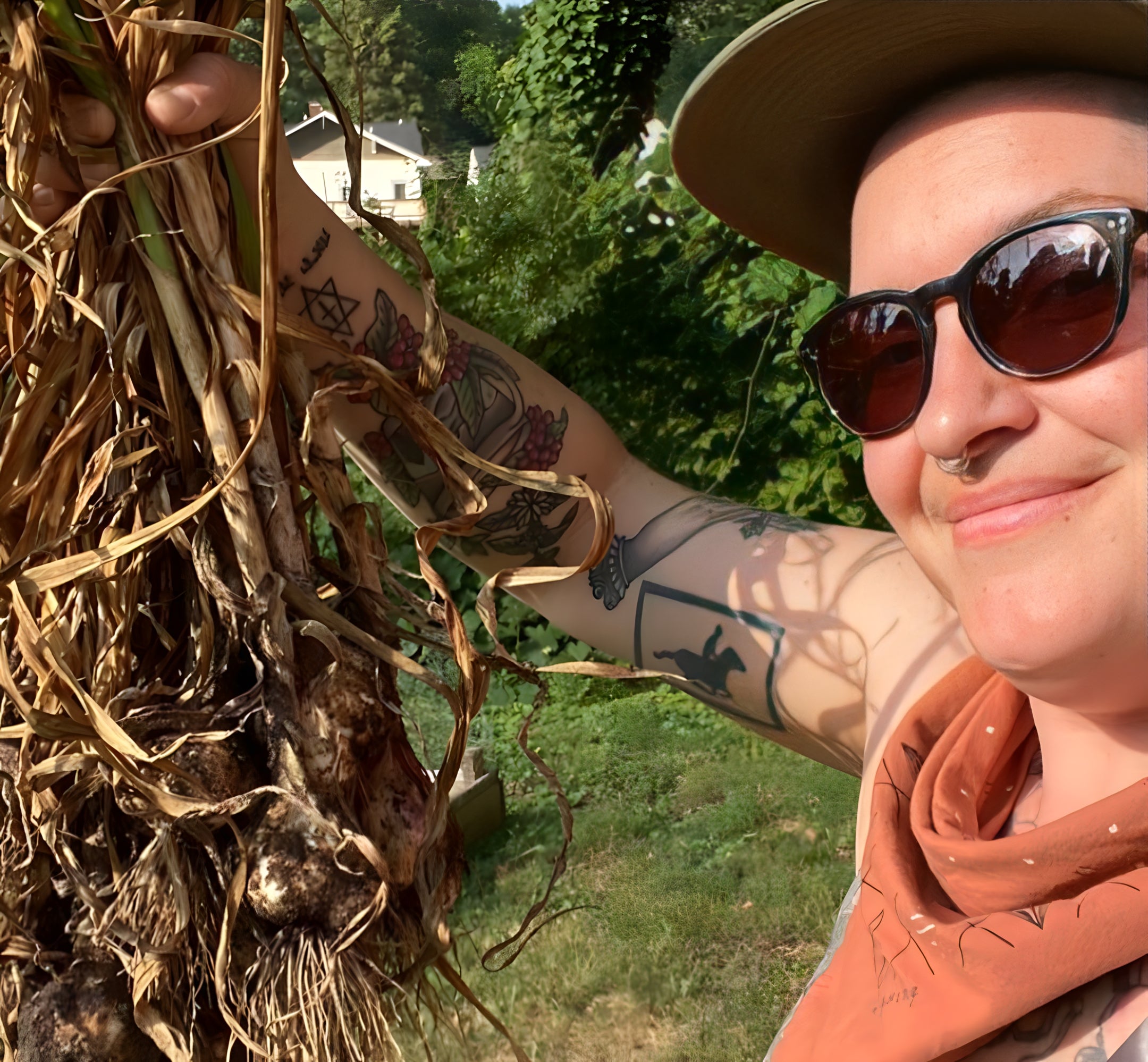 person in the garden wearing a clay-red jenni earle bandana from the self care club collection holding vegetables and smiling at the camera