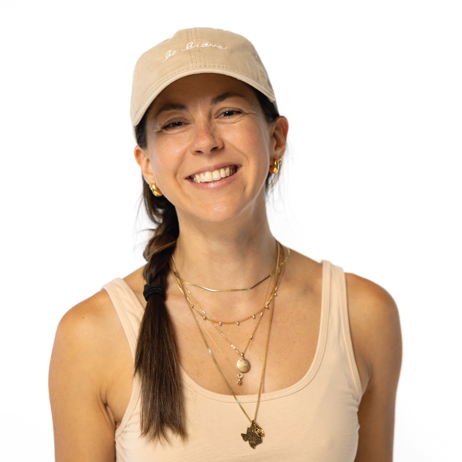 Woman wearing a beige cap with "be brave" embroidered on it and tank top with multiple necklaces