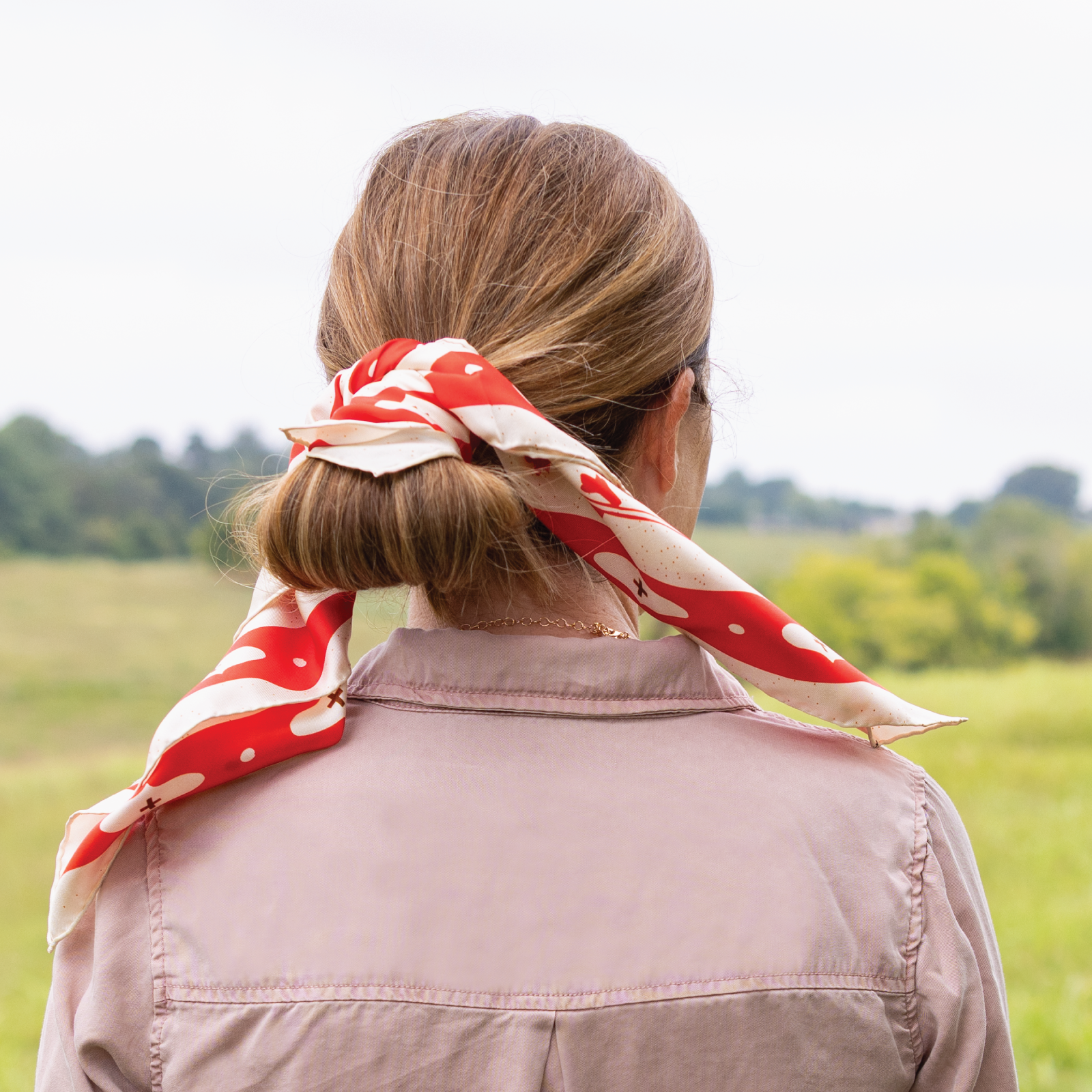 Person wearing a red and cream patterned silk headscarf in a field