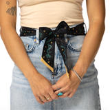 Person wearing a black silk twilly belt tied in a bow over blue jeans on a white background
