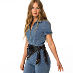 Woman wearing a denim jumpsuit with a black silk scarf as a belt on a white background
