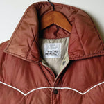 A rust-brown quilted puffer vest with white contrast stitching, snap-button front, and two front flap pockets