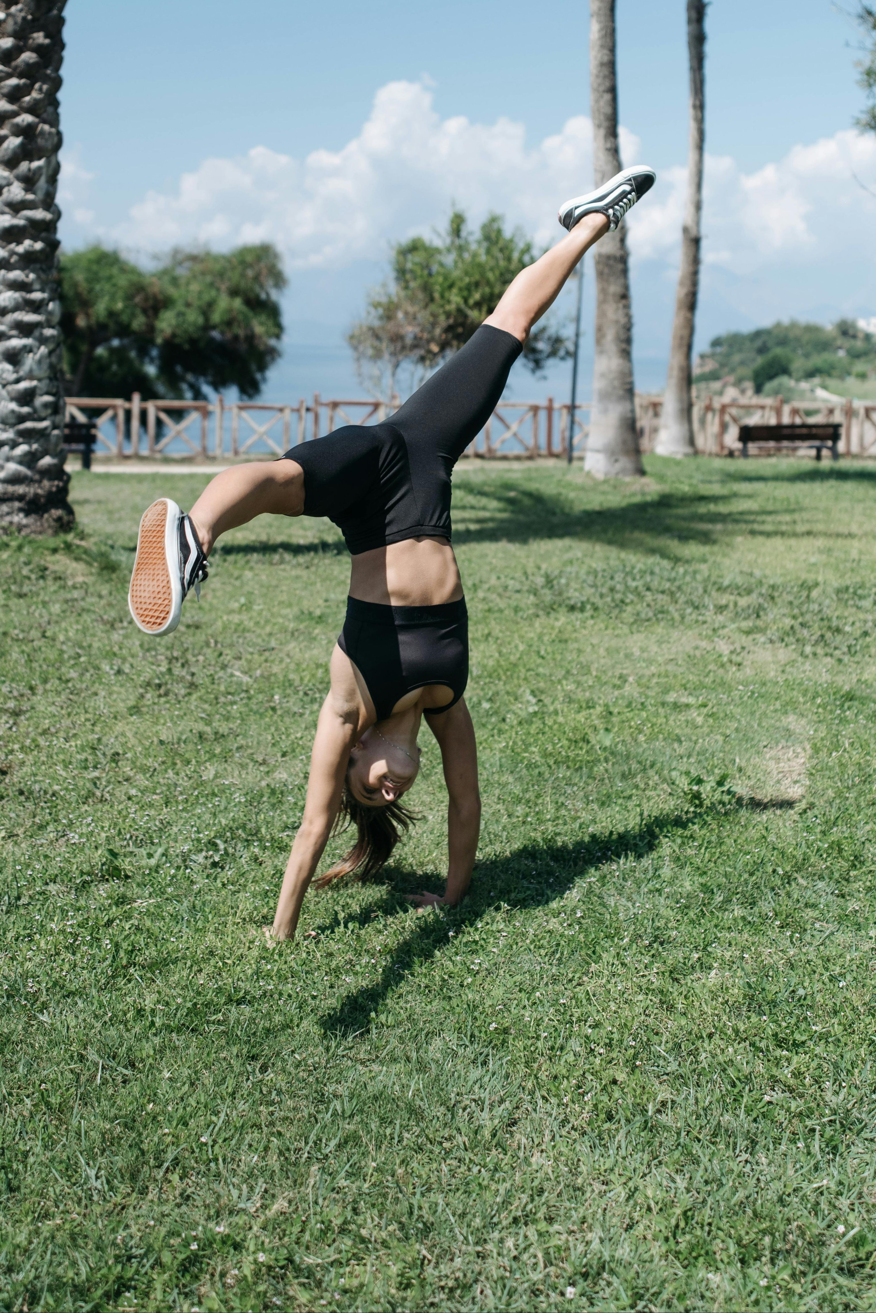 Person doing a handstand on grass with palm trees in the background